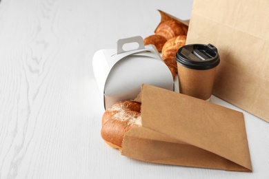 Paper bag with pastry and takeaway food on wooden table. Space for text