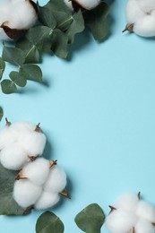 Photo of Cotton flowers and eucalyptus leaves on light blue background, flat lay. Space for text