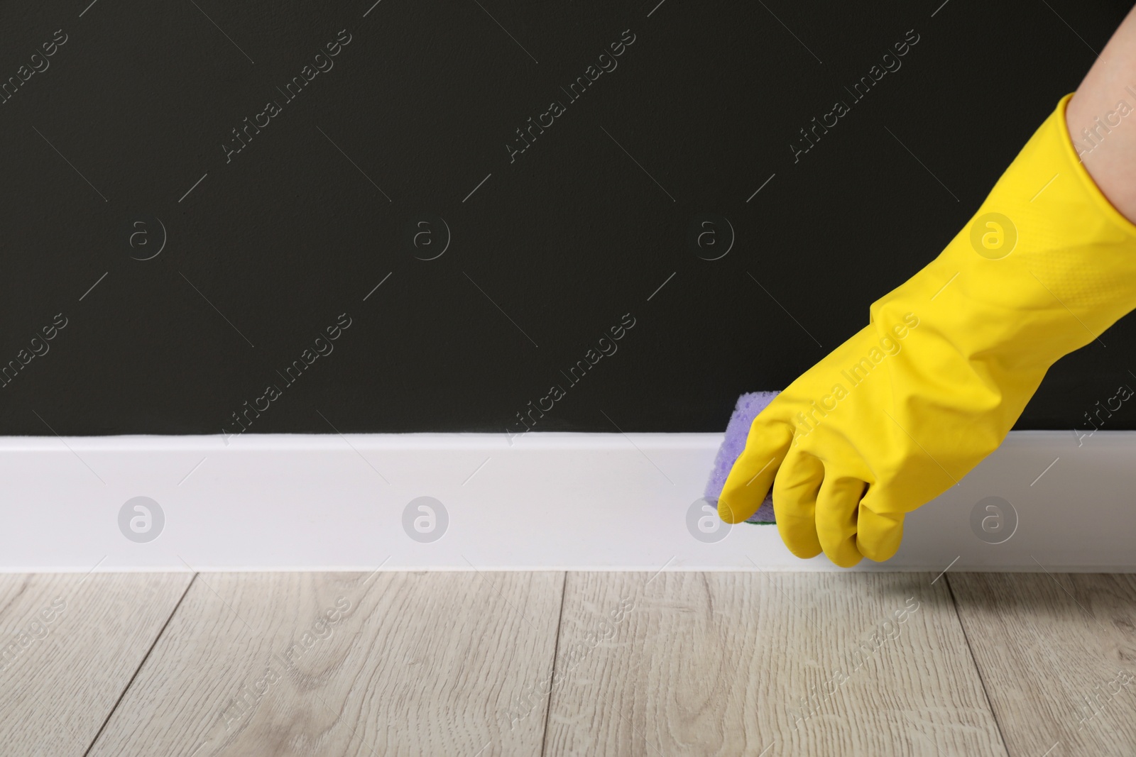 Photo of Woman in protective glove cleaning plinth with sponge indoors, closeup. Space for text