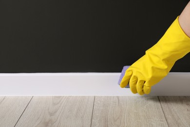 Woman in protective glove cleaning plinth with sponge indoors, closeup. Space for text