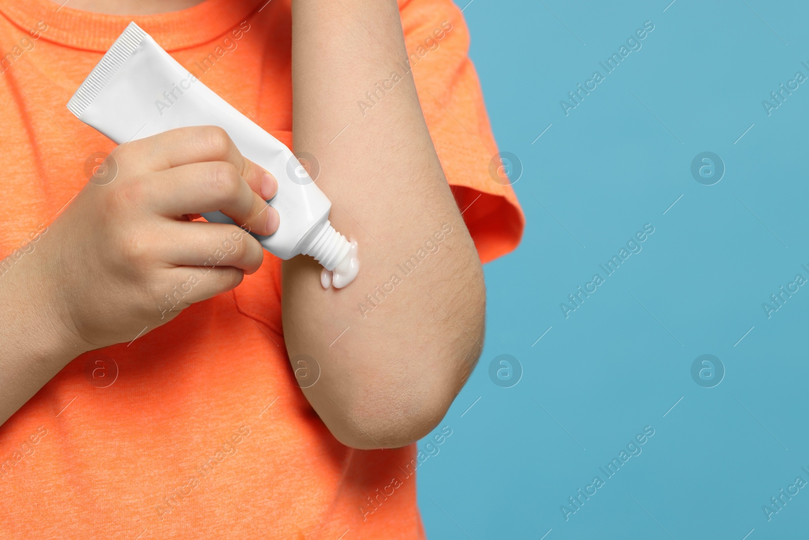 Photo of Child applying ointment onto elbow against light blue background, closeup. Space for text