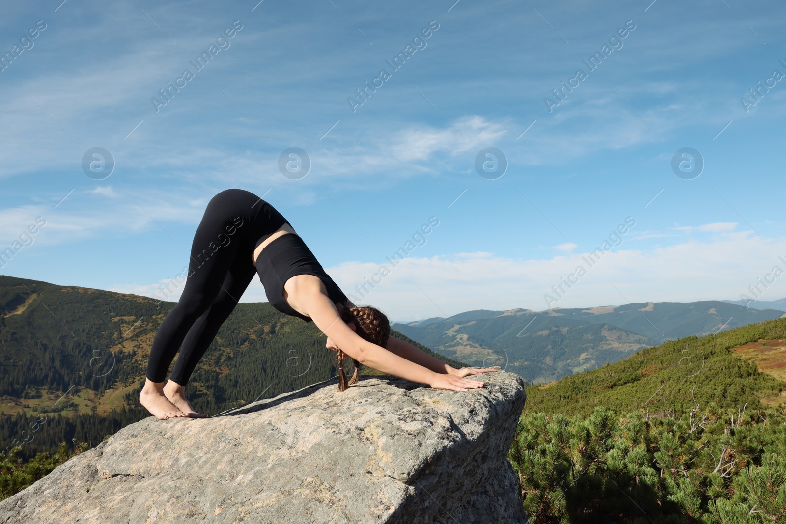 Photo of Beautiful young woman practicing yoga on rock in mountains