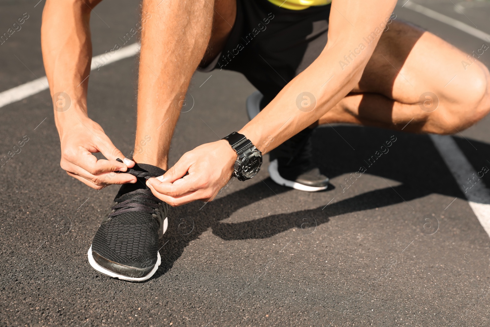 Photo of Young man tying shoelaces at stadium on sunny day