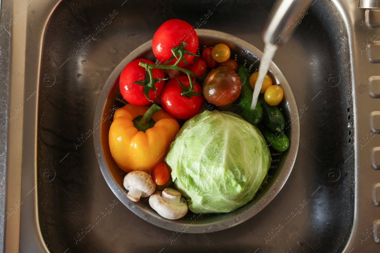 Photo of Washing different vegetables with tap water in metal colander inside sink, top view