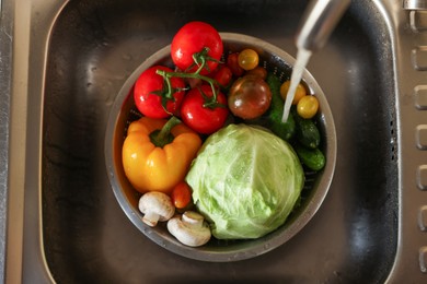 Washing different vegetables with tap water in metal colander inside sink, top view