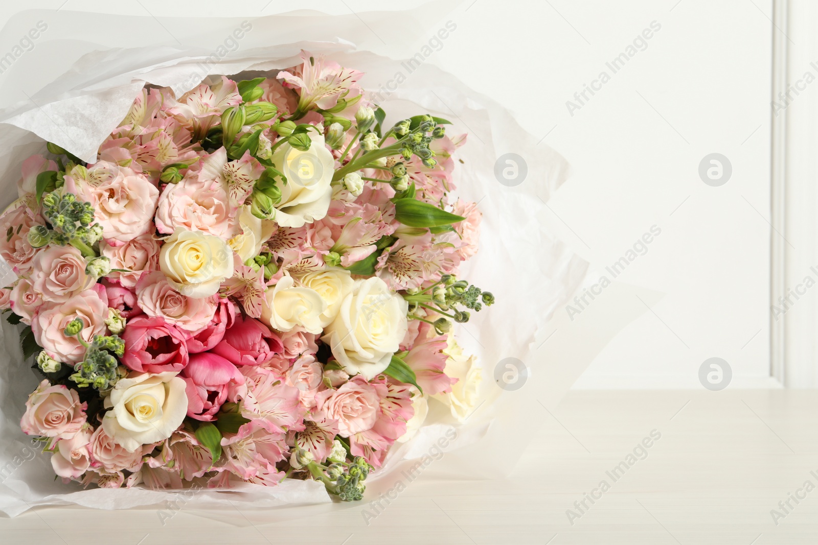 Photo of Beautiful bouquet of fresh flowers on wooden table near white wall, space for text