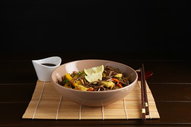 Photo of Stir-fry. Delicious cooked noodles with chicken and vegetables in bowl served on wooden table against dark background, space for text