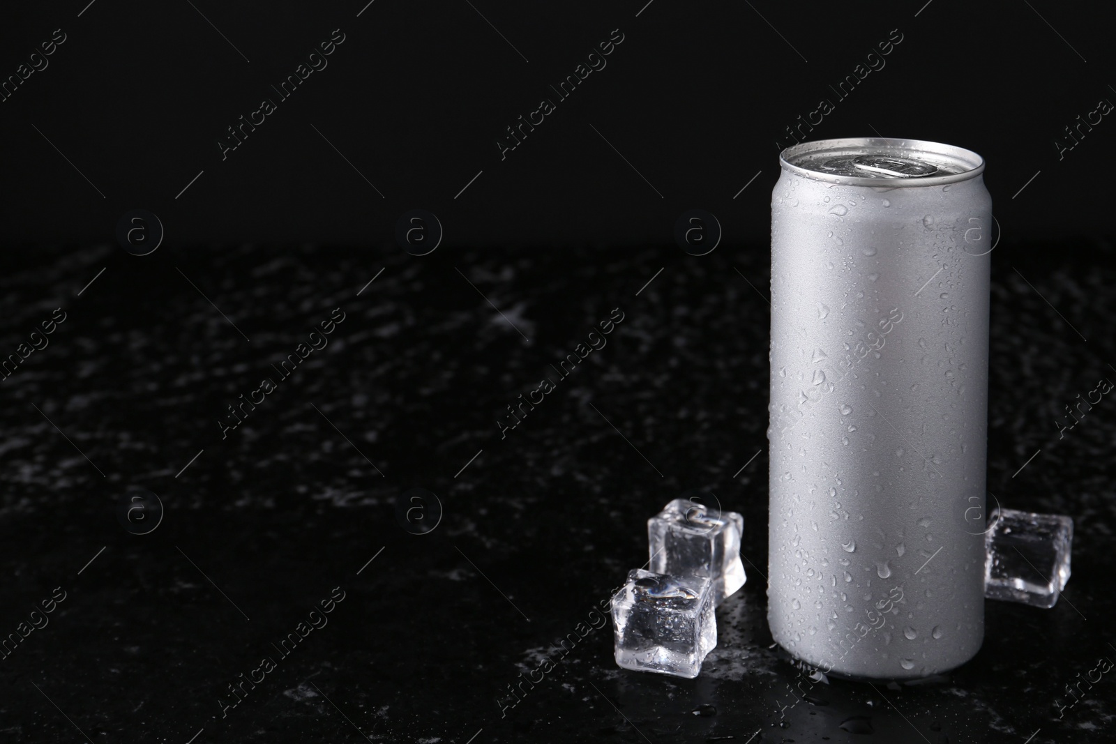 Photo of Energy drink in wet can and ice cubes on black textured table, space for text