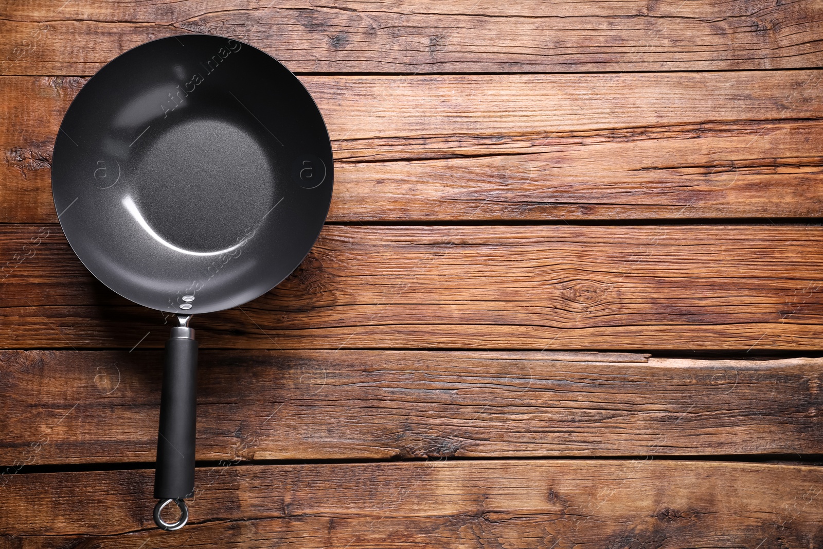 Photo of Empty iron wok on wooden table, top view. Space for text