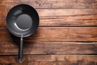 Empty iron wok on wooden table, top view. Space for text