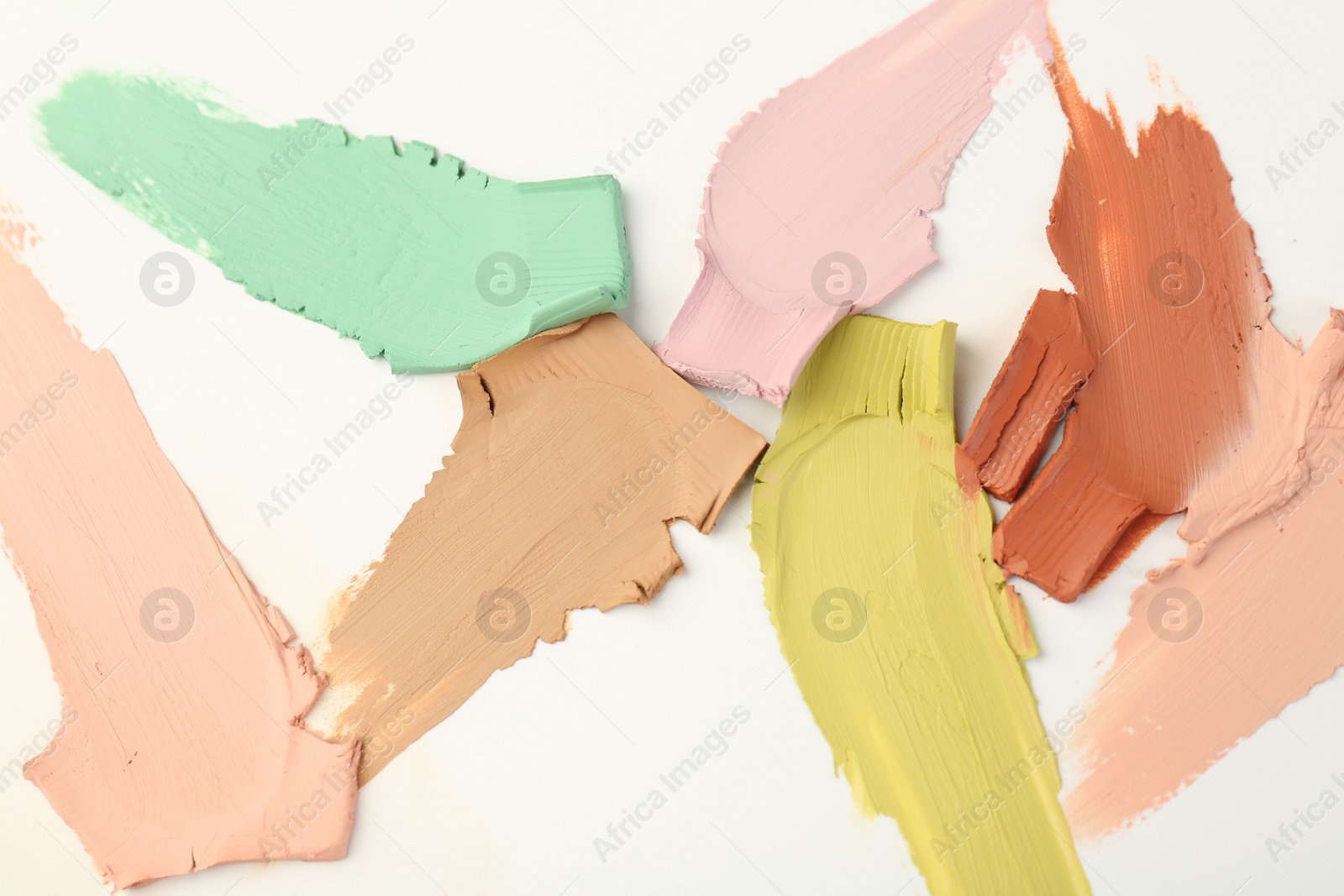 Photo of Samples of different color correcting concealers on white background, top view