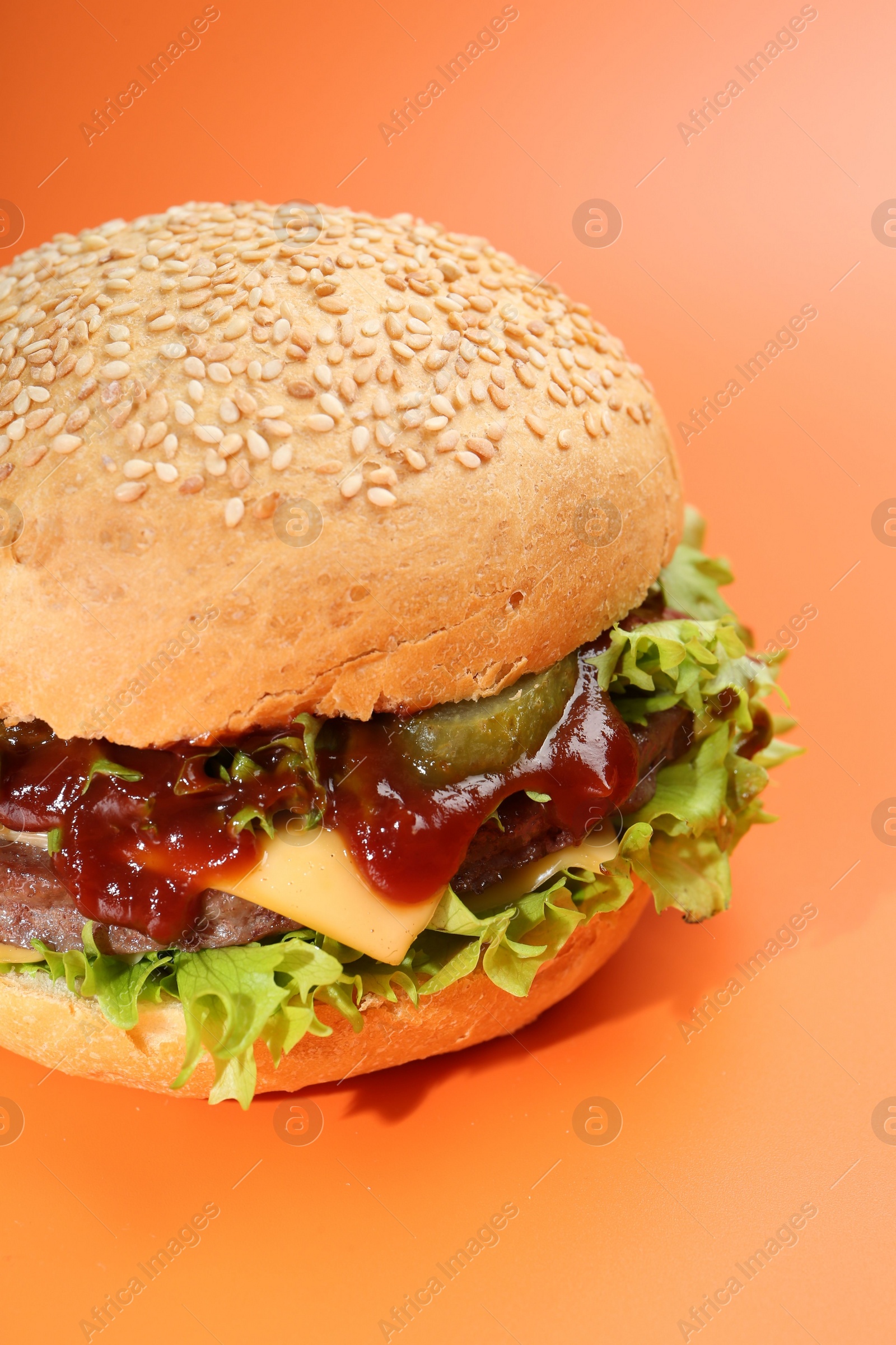 Photo of Delicious cheeseburger with lettuce, pickle, ketchup and patty on coral background, closeup