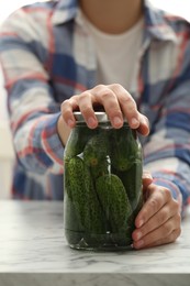 Photo of Woman pickling glass jar of cucumbers at white marble table, closeup