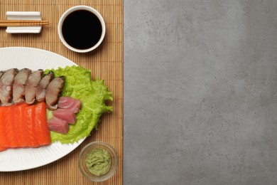 Photo of Delicious mackerel, salmon and tuna served with lettuce, wasabi and soy sauce on grey table, top view. Space for text. Tasty sashimi dish