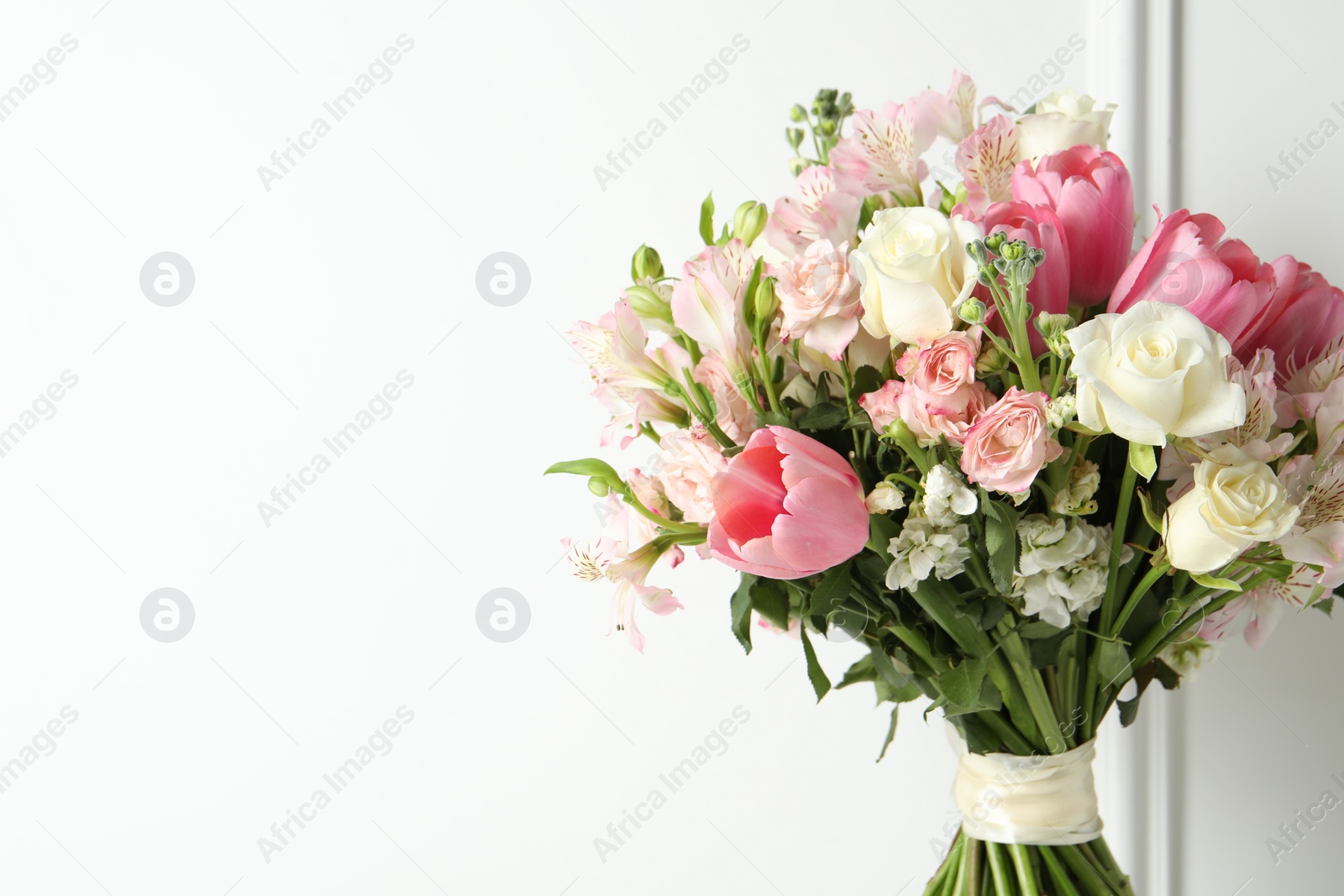 Photo of Beautiful bouquet of fresh flowers near white wall. Space for text