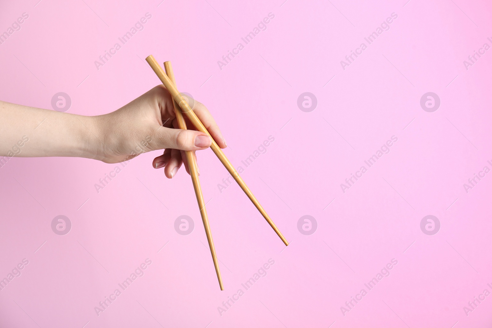 Photo of Woman holding pair of wooden chopsticks on pink background, closeup. Space for text