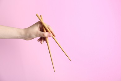 Woman holding pair of wooden chopsticks on pink background, closeup. Space for text