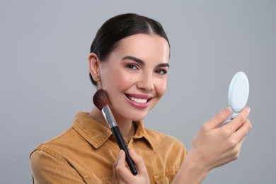 Photo of Happy woman with cosmetic pocket mirror applying makeup on light grey background