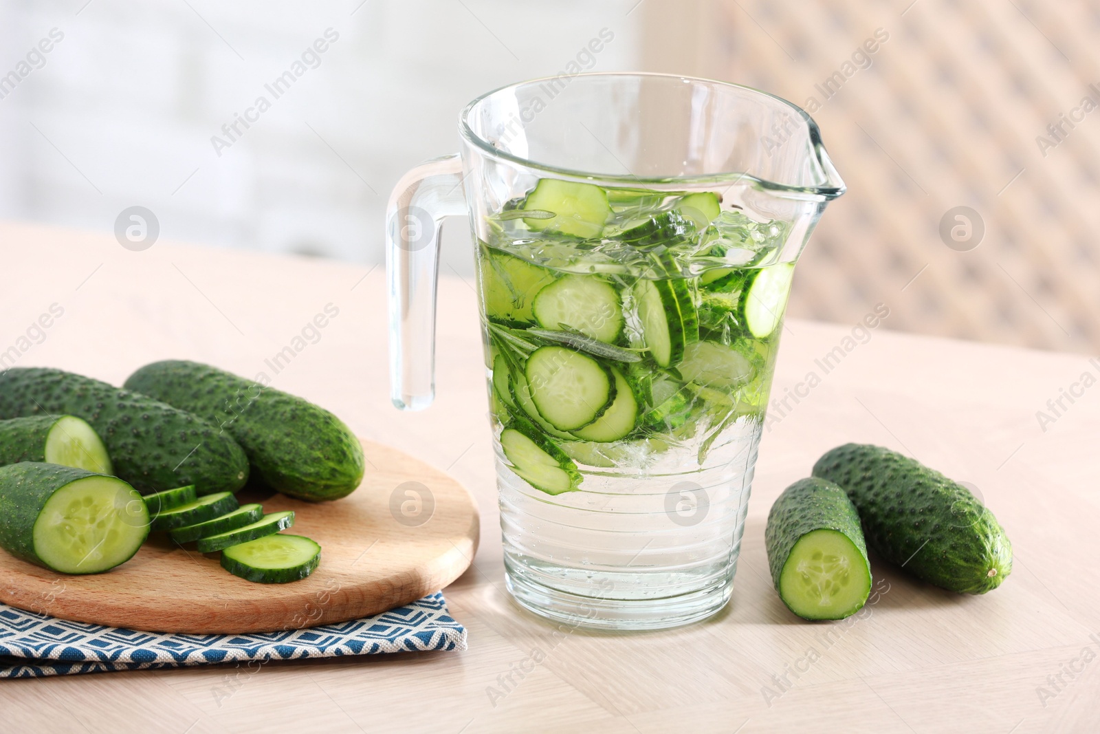 Photo of Refreshing cucumber water in jug and vegetables on light wooden table