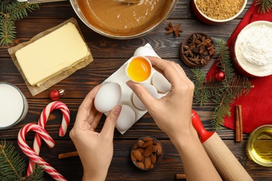 Photo of Woman cooking traditional Christmas cake at wooden table with ingredients, top view