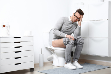 Photo of Man with stomach ache sitting on toilet bowl in bathroom