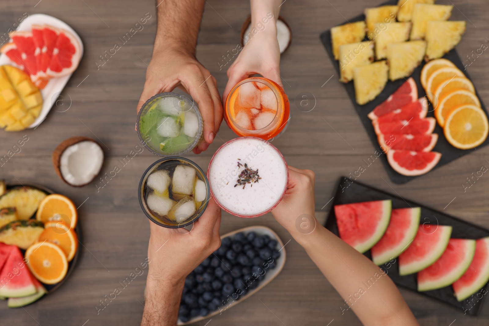 Photo of Friends clinking glasses with cocktails at wooden table, top view