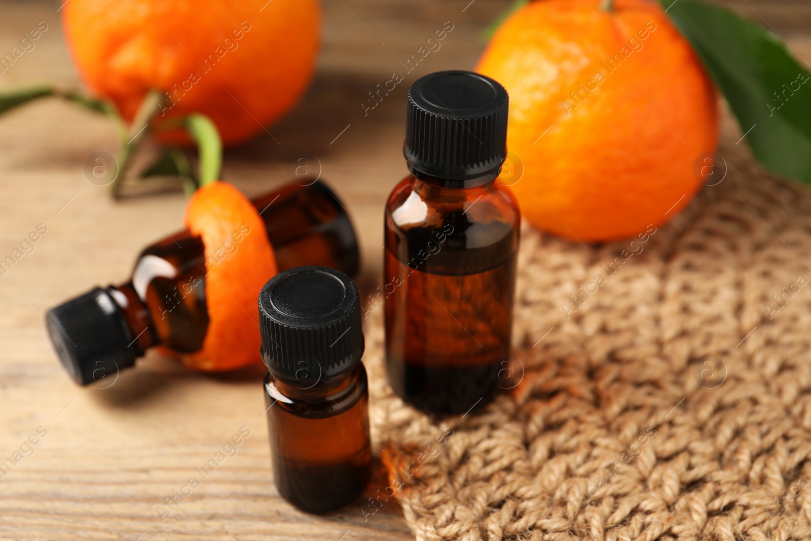 Photo of Bottles of tangerine essential oil, fresh fruit and peel on wooden table, closeup