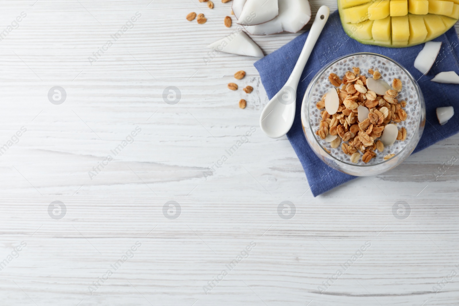 Photo of Delicious chia pudding with granola and mango on white wooden table, flat lay. Space for text