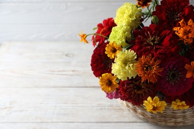 Photo of Beautiful wild flowers in wicker basket on light wooden table, closeup. Space for text