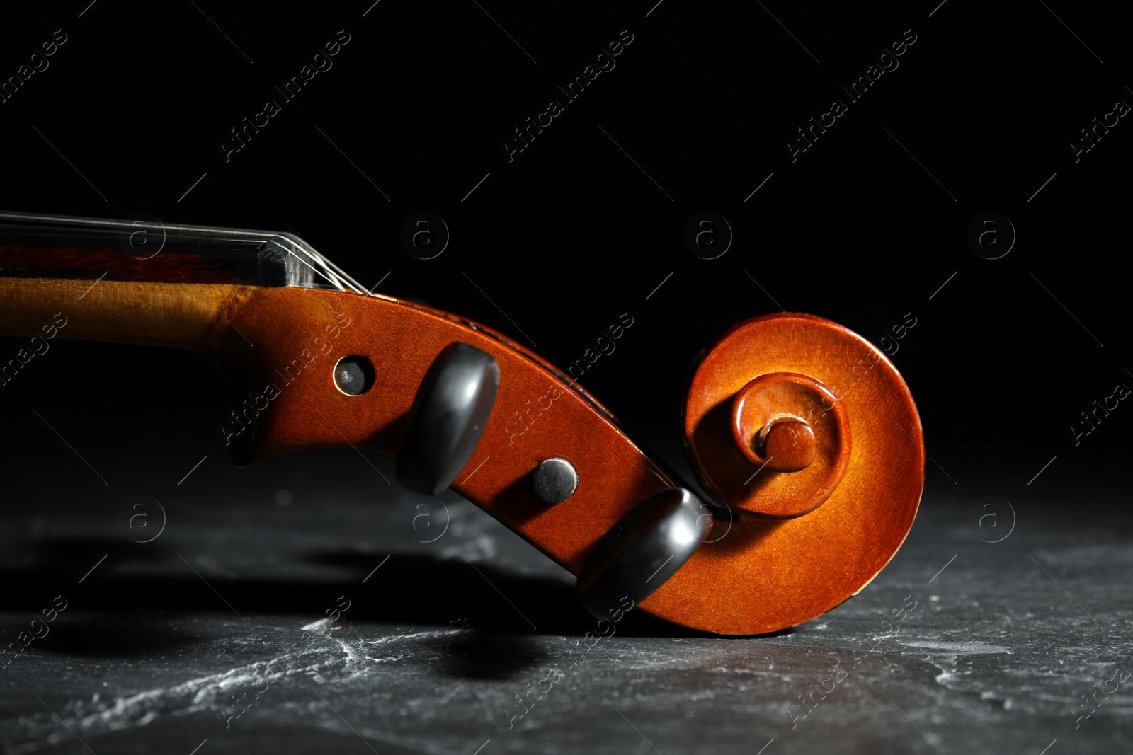 Photo of Classic violin on stone table against black background, closeup