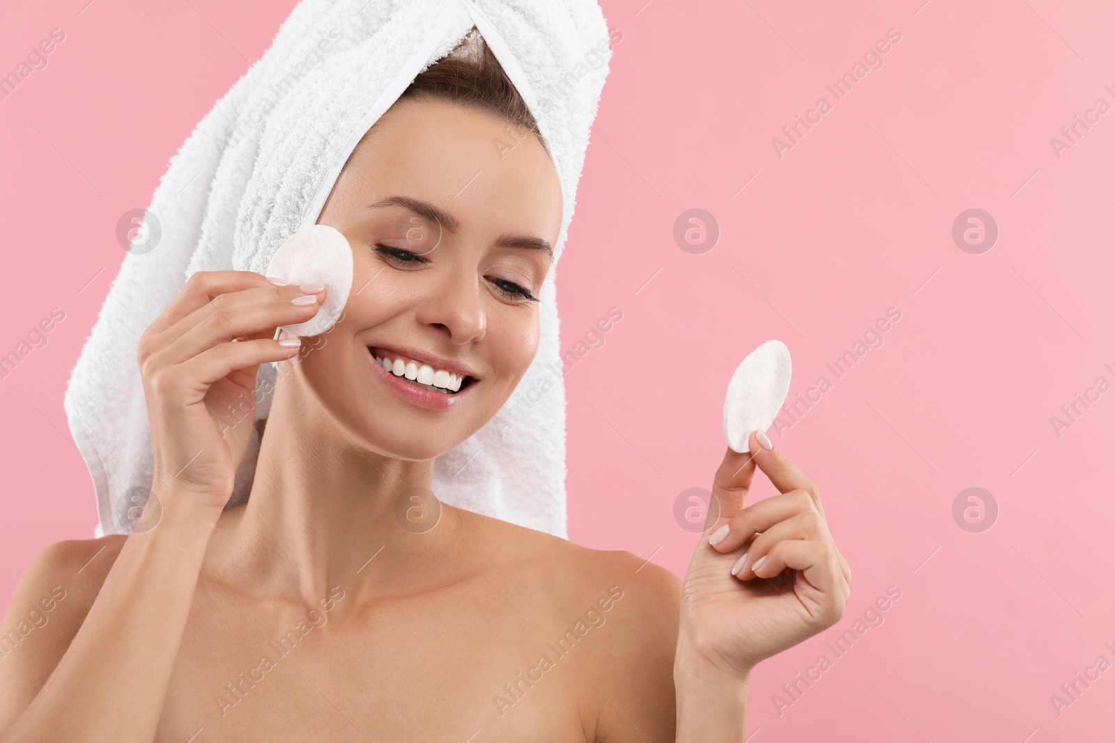 Photo of Smiling woman removing makeup with cotton pads on pink background