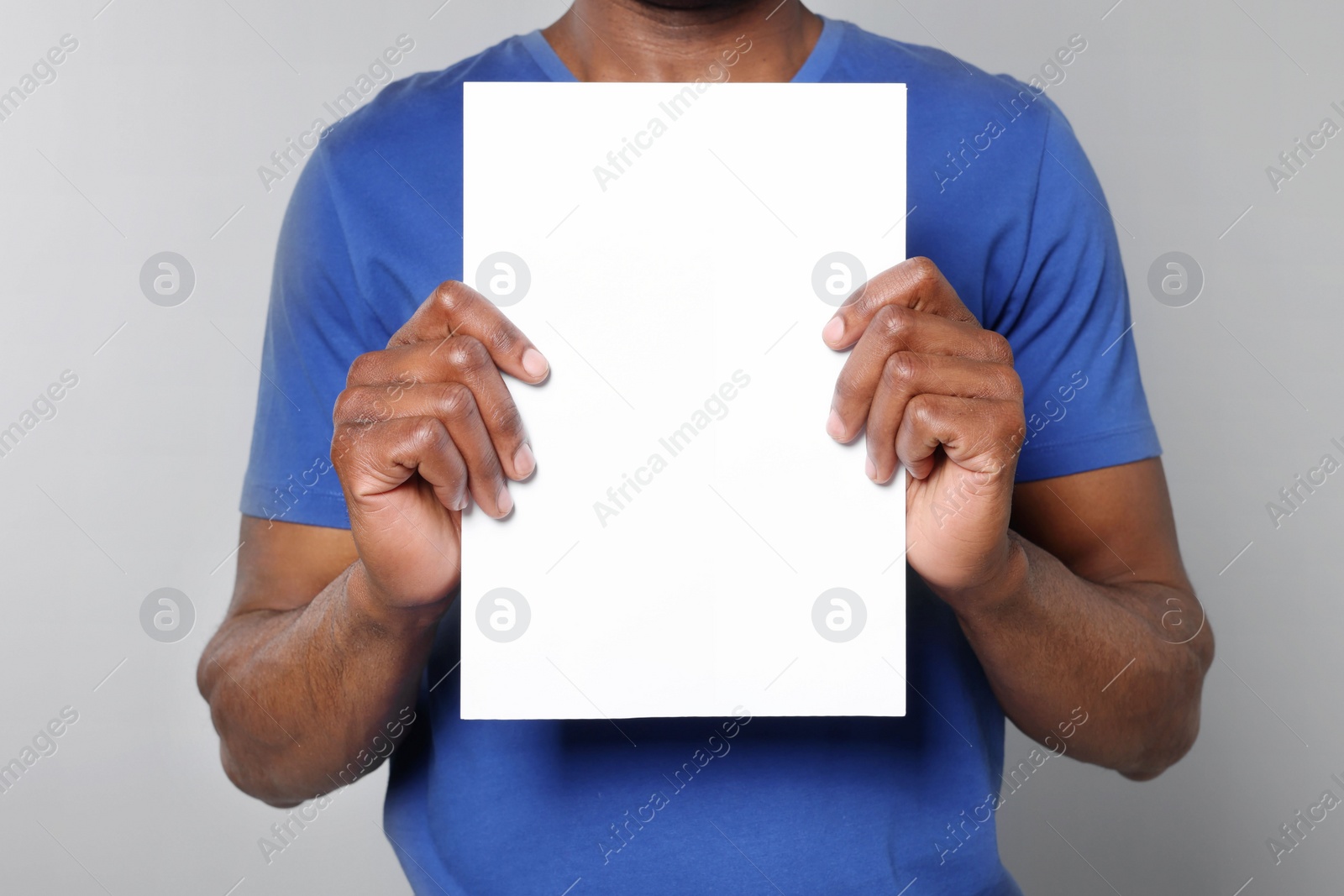 Photo of African American man holding sheet of paper on grey background, closeup. Mockup for design