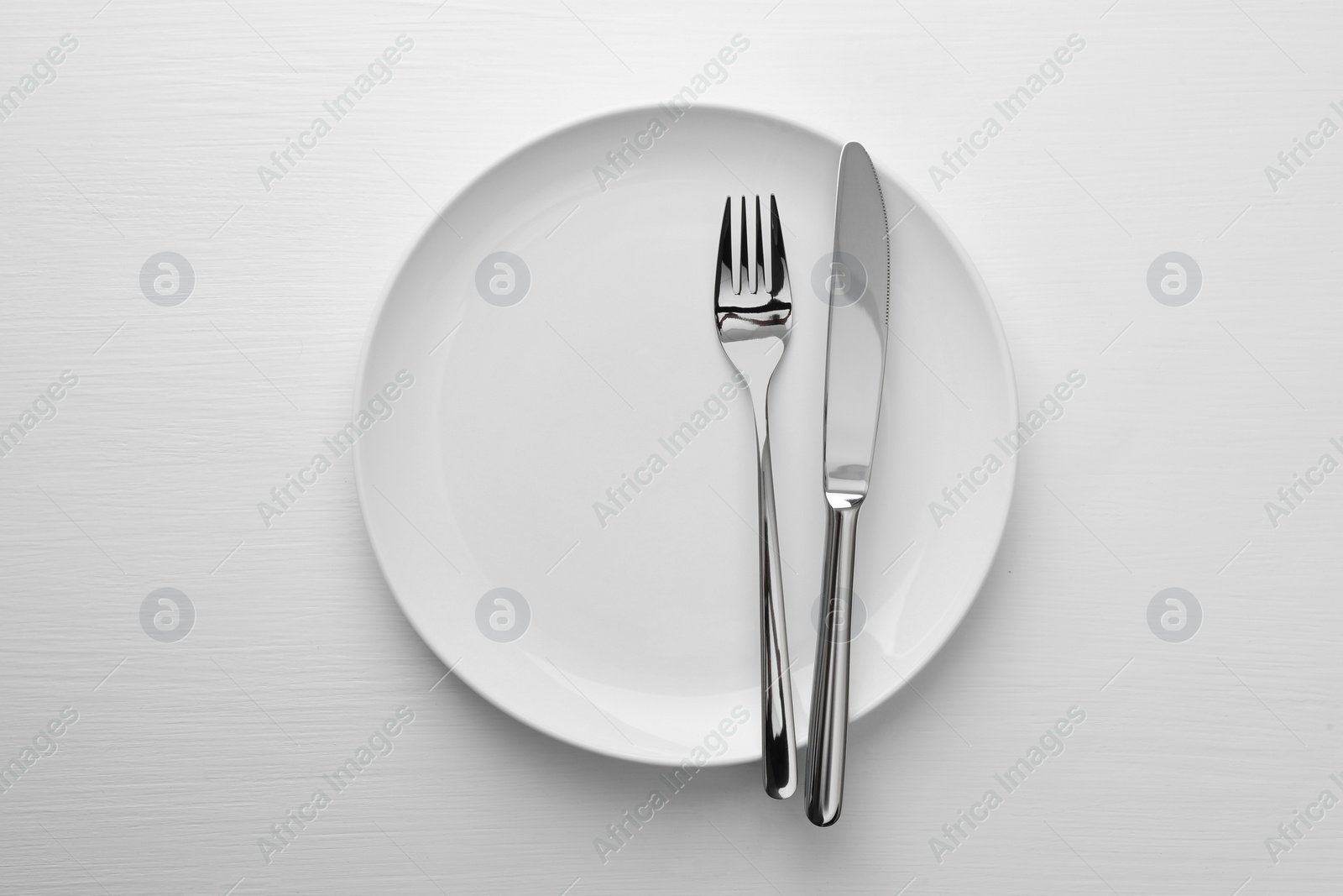 Photo of Clean plate, fork and knife on white table, top view