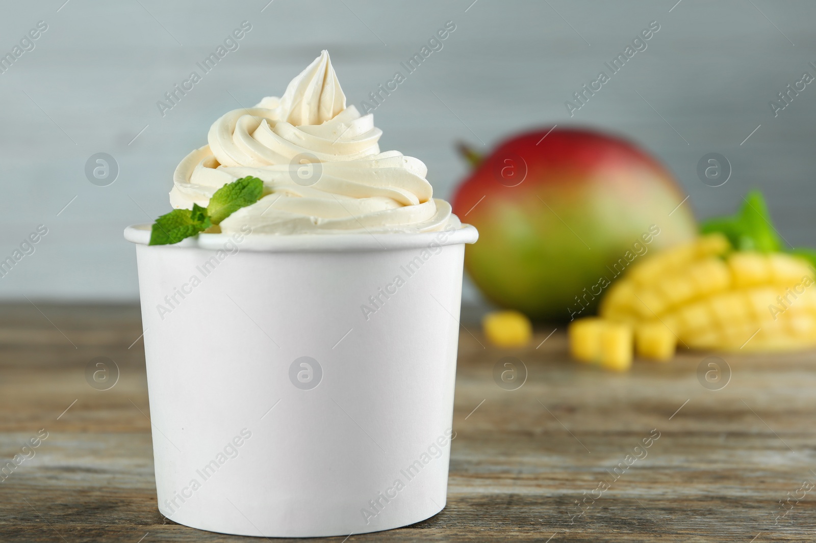 Photo of Cup with tasty frozen yogurt and mango on wooden table. Space for text