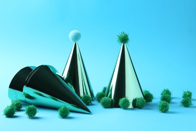 Photo of Party hats with green pompoms on light blue background