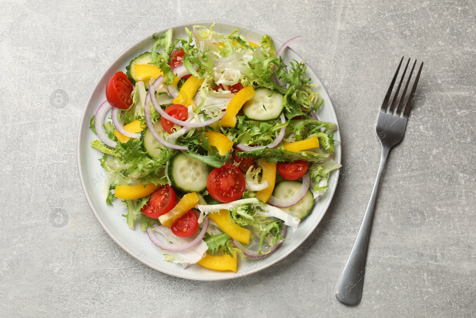 Photo of Tasty fresh vegetarian salad and fork on grey table, top view