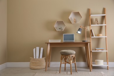 Photo of Comfortable wooden stool near table with laptop indoors. Interior design