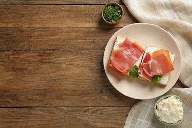 Delicious sandwiches with cream cheese and jamon on wooden table, flat lay. Space for text