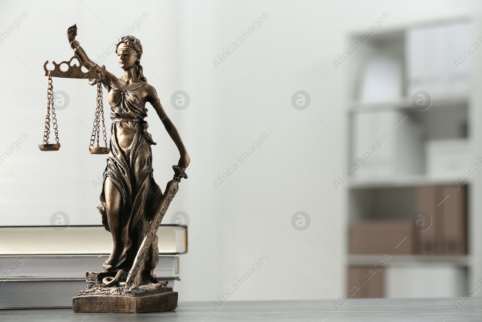 Photo of Figure of Lady Justice and books on table indoors, space for text. Symbol of fair treatment under law