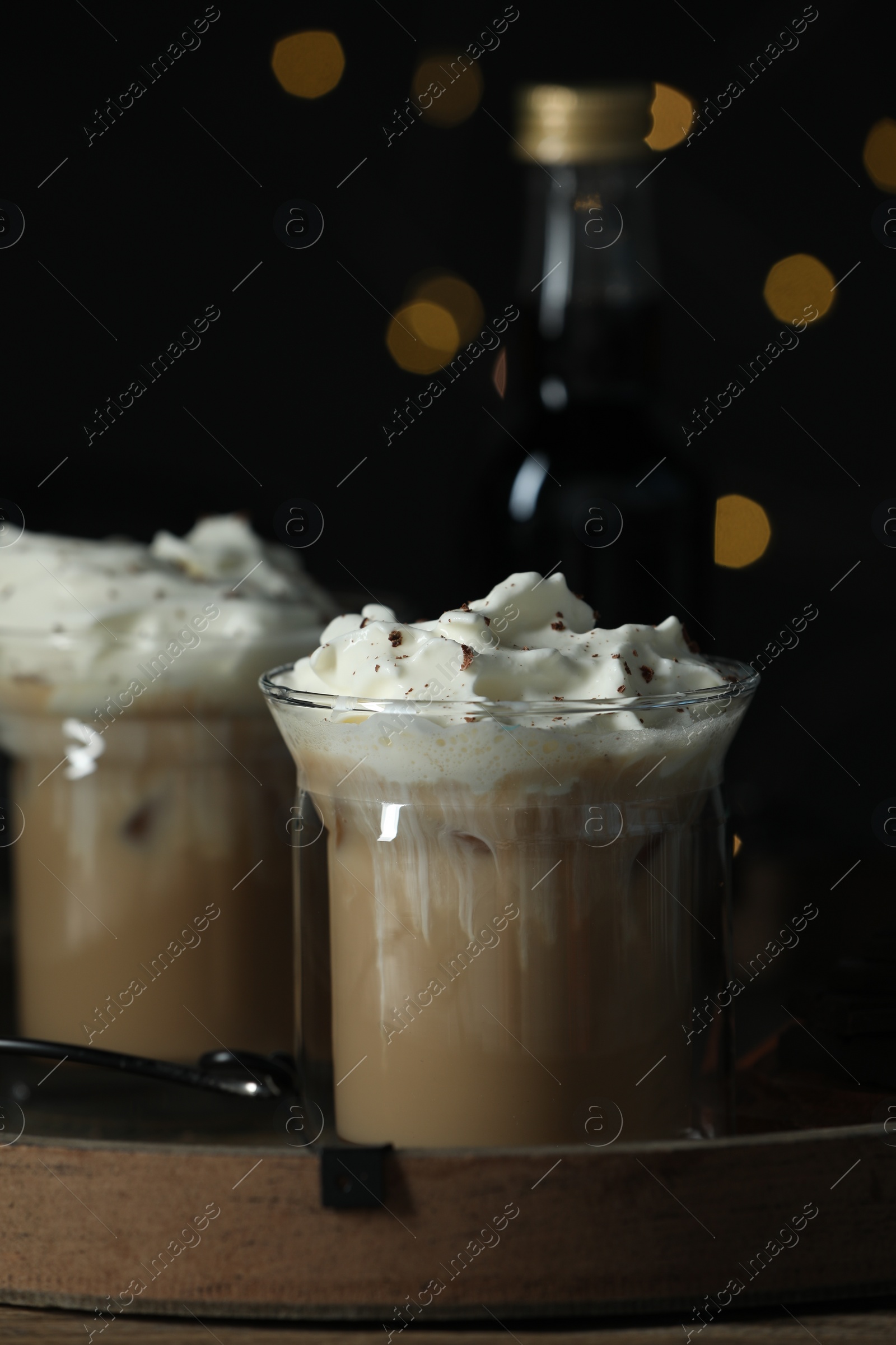 Photo of Glasses of iced coffee and bottle of syrup against blurred lights, closeup