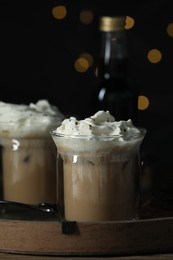 Glasses of iced coffee and bottle of syrup against blurred lights, closeup