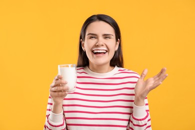 Happy woman with milk mustache holding glass of tasty dairy drink on yellow background