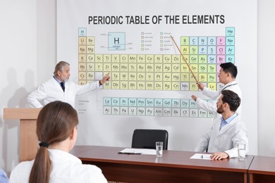 Image of Lecture in chemistry. Professors using projection screen with illustration of periodic table to audience in conference room