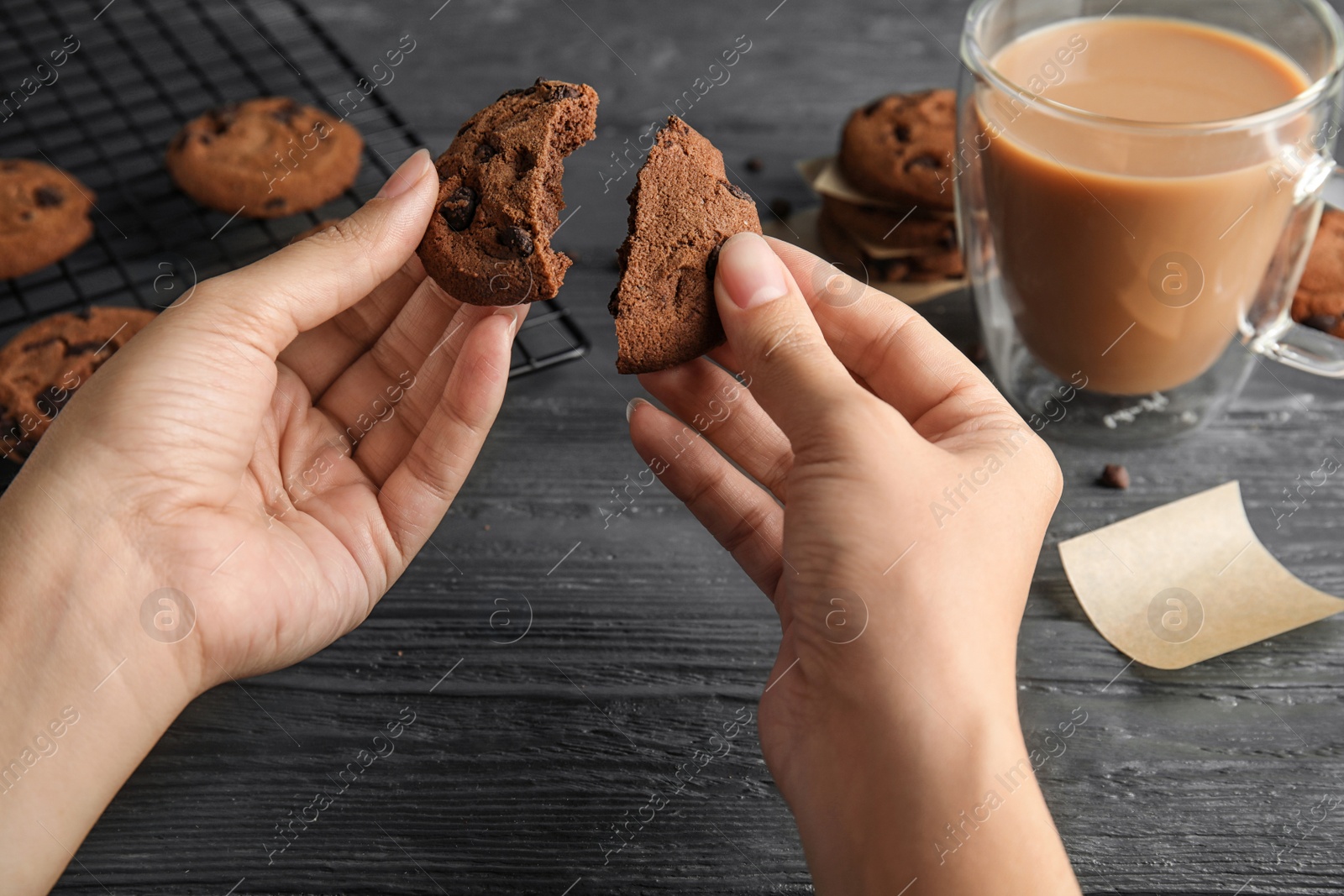 Photo of Woman holding tasty chocolate chip cookie over wooden table