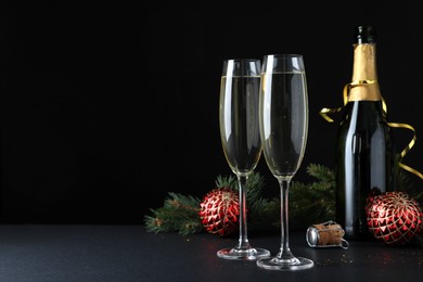 Photo of Happy New Year! Bottle of sparkling wine, glasses and festive decor on table against black background, space for text