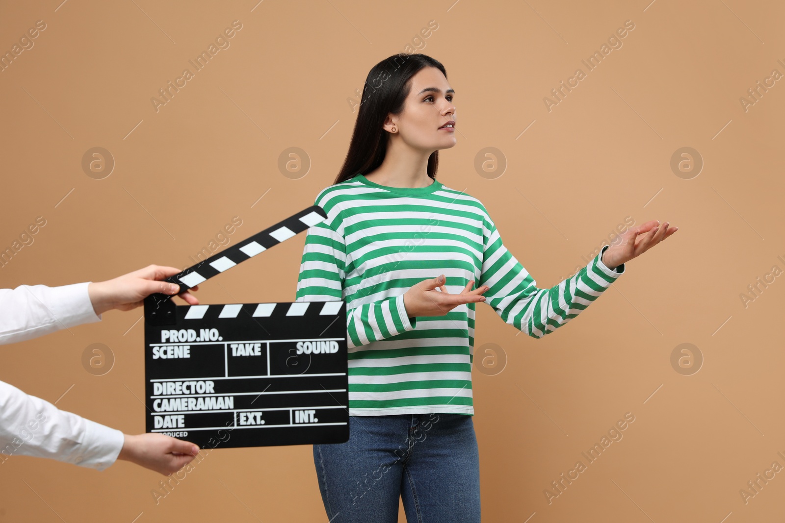 Photo of Actress performing while second assistant camera holding clapperboard on beige background. Film industry