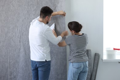 Woman and man hanging gray wallpaper in room, back view