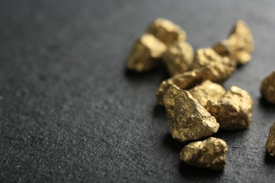 Photo of Shiny gold nuggets on grey textured surface, closeup. Space for text