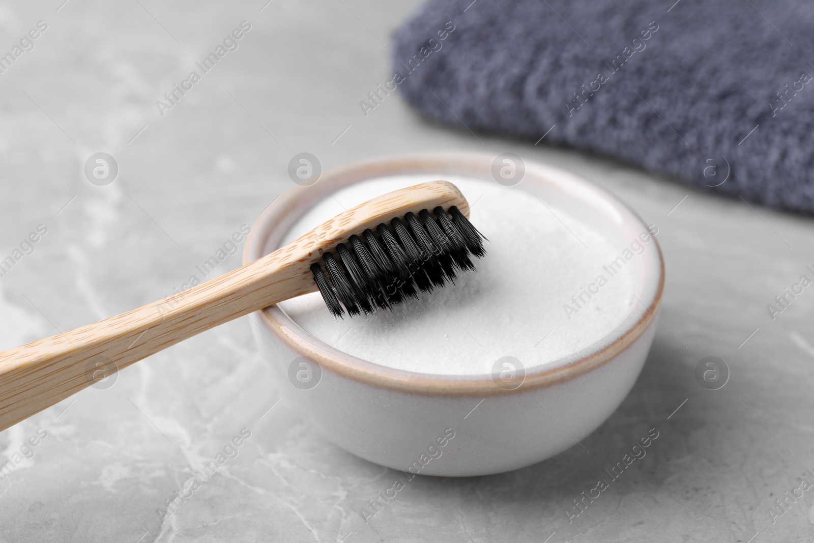 Photo of Bamboo toothbrush and bowl of baking soda on light grey table, closeup