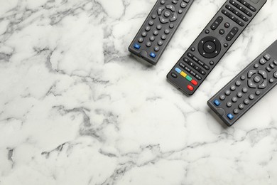 Photo of Modern tv remote controls on white marble table, flat lay. Space for text